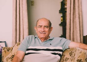A cheerful elderly man enjoys a relaxed moment on a sofa in a warmly decorated living room.